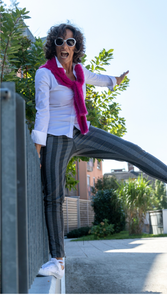 woman enjoying walking in her neighborhood. She has curly grey hair and striped pants with a pink scarf. 