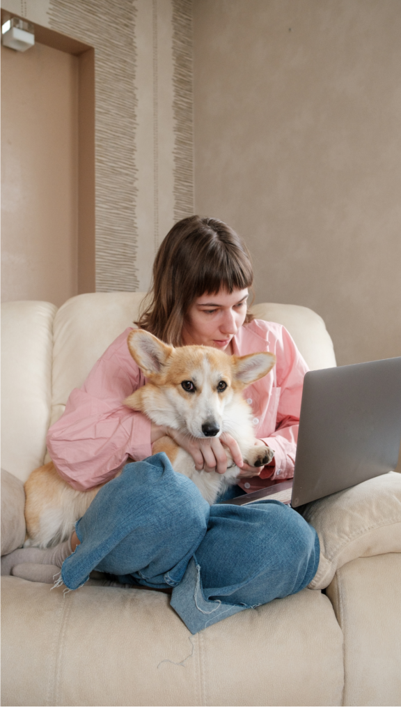 white woman holding blond dog as she works from her couch on her laptop