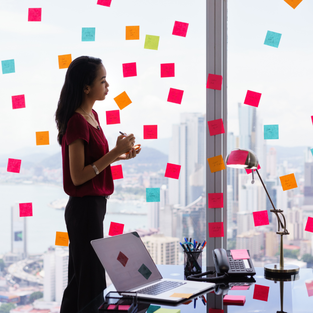 woman using the how to decide where to live sticky note method. She is in an office with sticky notes all over the glass wall. location must haves