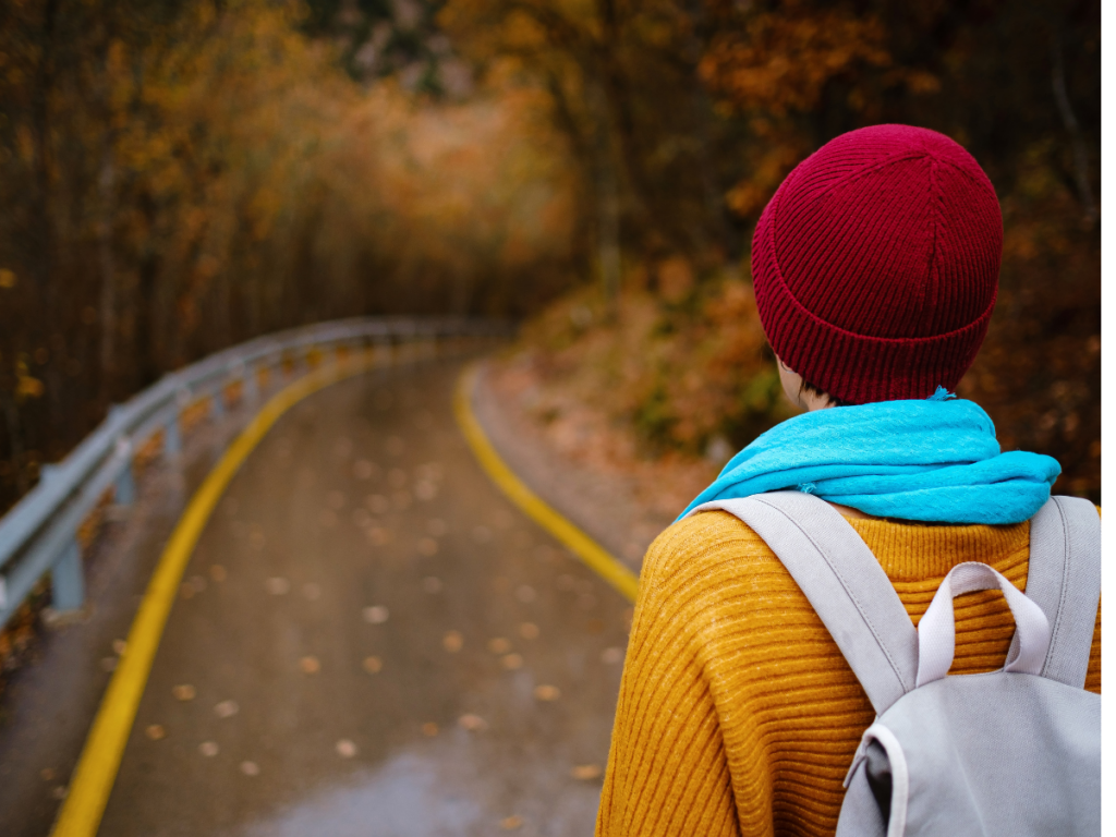 Girl dressed in a yellow sweater with a red beanie on walking down the street. the picture is inquisitive and she is on her location scouting journey to figure out where she wants to live.